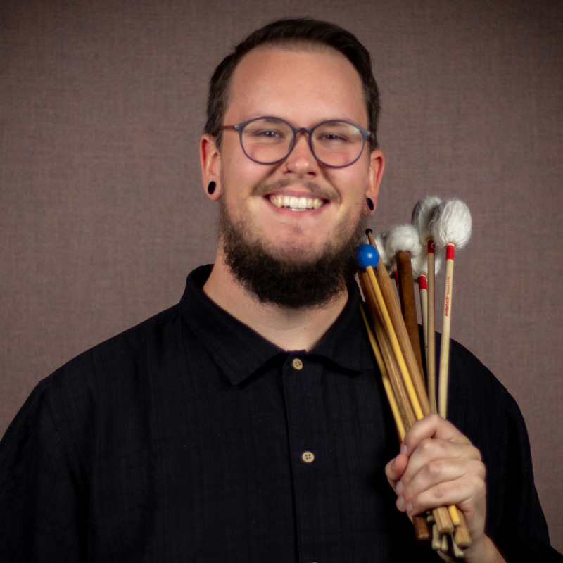 Photo of Taylor Smith, holding drumsticks, drum instructor and teacher at The Lesson Studio.